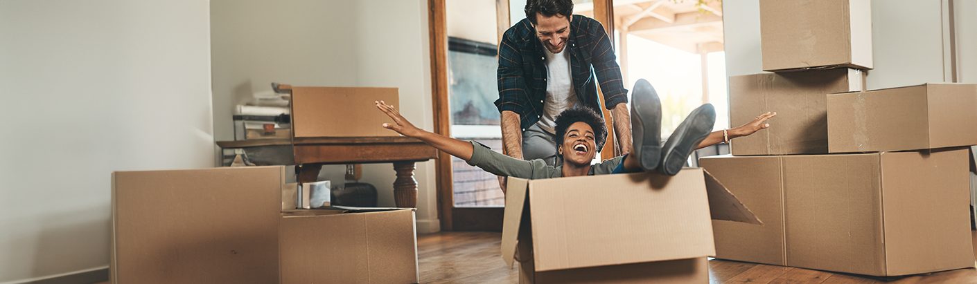 Excited man pushing a woman around the floor in an empty moving box in their new home.